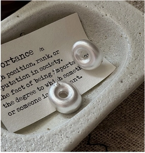 Close-up of minimalist matte silver hollow hoop earrings on a textured stone tray