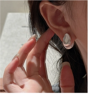 Detailed view of silver liquid metal teardrop earrings worn on a model's ear