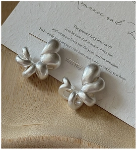 Detail of matte silver twisted knot stud earrings on vintage artistic card paper