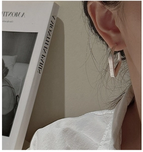 Détail de boucles d'oreilles créoles géométriques en argent mat portées par un modèle