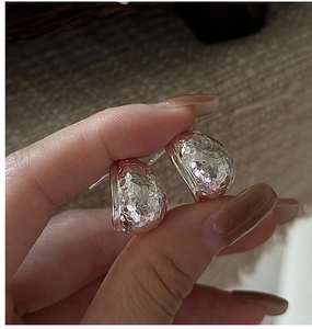 Detail of hand holding a textured hammered silver stud earring with polished finish