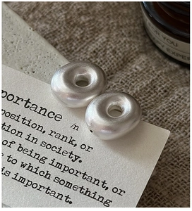 Close-up of matte silver hollow donut earrings on a white prop card and linen background