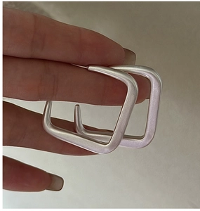 Détail de grandes boucles d'oreilles carrées en argent avec finition métal mat