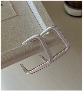 Détail de créoles carrées en argent 925 brossé mat sur un plateau en toile de coton