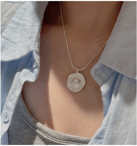 Macro detail of minimalist S925 sterling silver matte round pendant on snake chain necklace