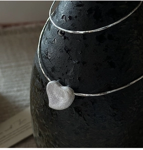 Macro detail of S925 sterling silver heart necklace with matte brushed metal texture
