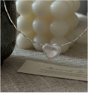 Macro detail of silver heart pendant with brushed texture on elegant square link chain