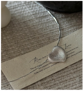 Macro detail of silver heart pendant with brushed matte finish on a delicate snake chain