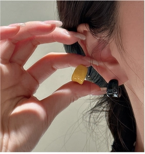 Dettaglio di orecchini a cerchio a C minimalisti lucidi in colori nero e giallo