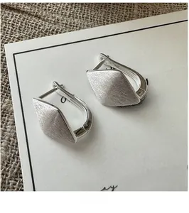 Close-up of brushed S925 sterling silver rhombic hoop earrings on a vintage linen backdrop