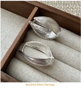 Macro detail of silver leaf hoop earrings with brushed texture and tiny zircon inlay