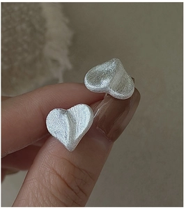 Macro detail of S925 silver heart stud earrings with matte brushed metallic texture