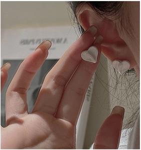 Macro shot of silver heart stud earrings featuring a minimalist brushed metallic texture