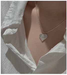 Détail d'un collier cœur en argent S925 avec texture martelée portée sur une chemise blanche