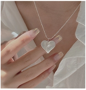 Détail macro d'un pendentif cœur vintage brossé sur une chaîne à billes en argent