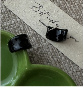 Dettaglio di orecchini neri lucidi a forma di C in argento su un piatto di ceramica