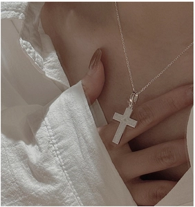 Close-up of minimalist brushed S925 sterling silver cross necklace on a white shirt