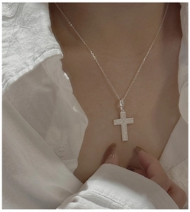 Close-up of minimalist S925 silver cross pendant with a brushed vintage metal texture