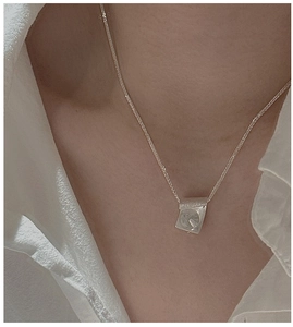 Close-up of S925 silver envelope necklace with brushed texture on white shirt background