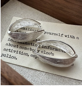 Macro view of S925 sterling silver earrings with textured leaf design on vintage paper