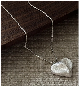 Vue détaillée du pendentif cœur en argent brossé mat sur une fine chaîne perlée