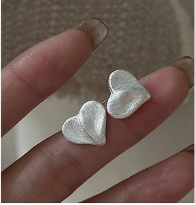 Macro shot of S925 sterling silver heart earrings with a brushed matte finish on fingertips