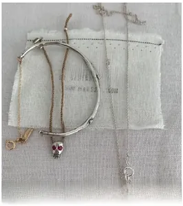 Detail of woven bracelet with skull charm and S925 silver bangles on white fabric