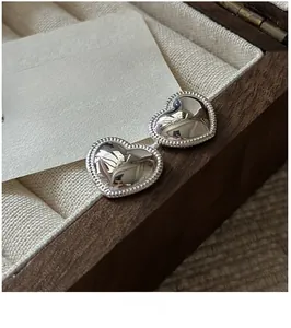 Close-up of heart-shaped S925 sterling silver earrings with beaded edges on a wooden box