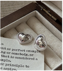 Macro view of silver heart-shaped stud earrings with bead edge on wooden jewelry box