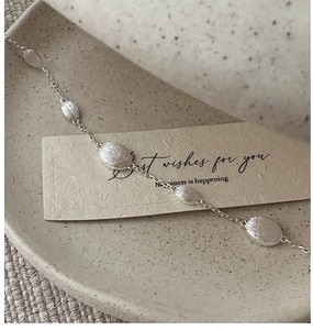 Detail of S925 sterling silver beaded bracelet with brushed oval charms on a ceramic tray