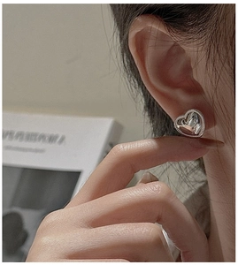 Detailed view of silver heart-shaped stud earring with wavy edges on a model's ear