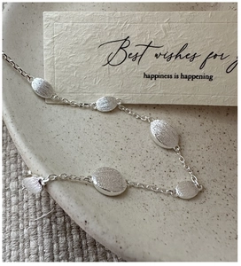 Macro detail of S925 sterling silver chain with brushed oval beads on ceramic plate