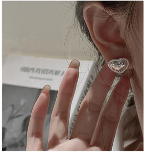 Macro detail of silver heart stud earring with textured vintage edge on female ear