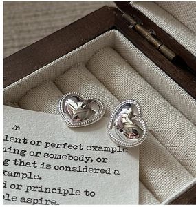 Macro shot of silver heart studs with beaded edges on a vintage wooden jewelry box cushion