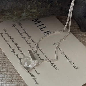 Elegant S925 silver necklace with matte folded pendant and clear crystal on textured fabric