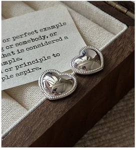 Macro detail of silver heart-shaped stud earrings with beaded edges on velvet lining
