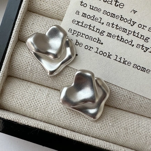 Orecchini a cuore in argento S925 opaco con design a doppio strato su tessuto beige