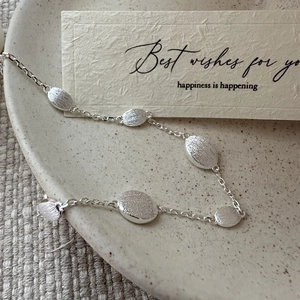 Minimalist S925 sterling silver bracelet with brushed oval beads on a ceramic plate