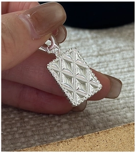 Macro detail of silver rhombic quilted pendant with beaded edges held by hand