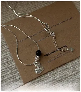 Close-up of S925 silver heart necklace with black agate bead on vintage card