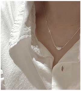Collier minimaliste en argent S925 avec pendentif haricot porté sur un chemisier blanc