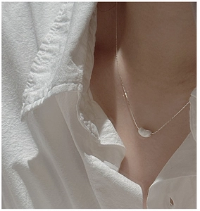 Détail d'un collier avec pendentif fève en argent sur un mannequin en chemise blanche