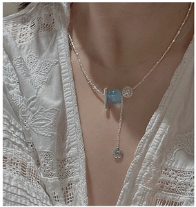 Détail du collier floral en argent avec perles bleues et barre sur fond de dentelle