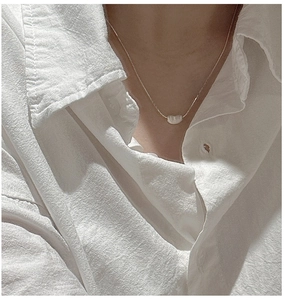 Gros plan d'un pendentif haricot en argent sur une chaîne fine portée sur une chemise