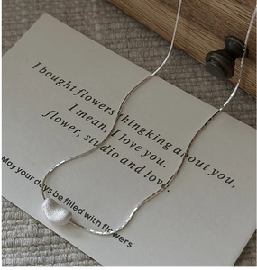 Détail du collier pendentif haricot en argent mat avec chaîne à facettes sur lin
