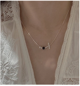 Close-up of S925 sterling silver chain with geometric bar and black bead on lace garment