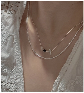 Close-up of layered S925 silver necklaces with black bead and T-pendant on lace fabric