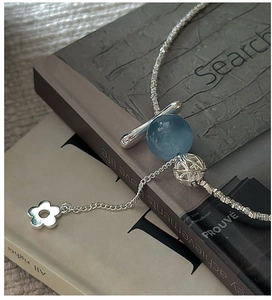 Détail du collier en argent S925 avec perle bleu clair et pendentif fleur sur livres anciens
