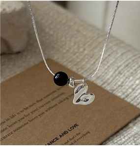 Macro detail of S925 silver necklace with black agate bead and polished heart pendant