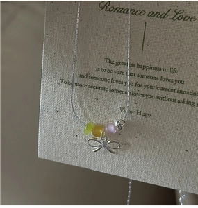 Detail of silver bow pendant with colorful translucent beads on a sleek chain necklace